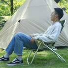 a man sitting on a lawn chair under a white tent 